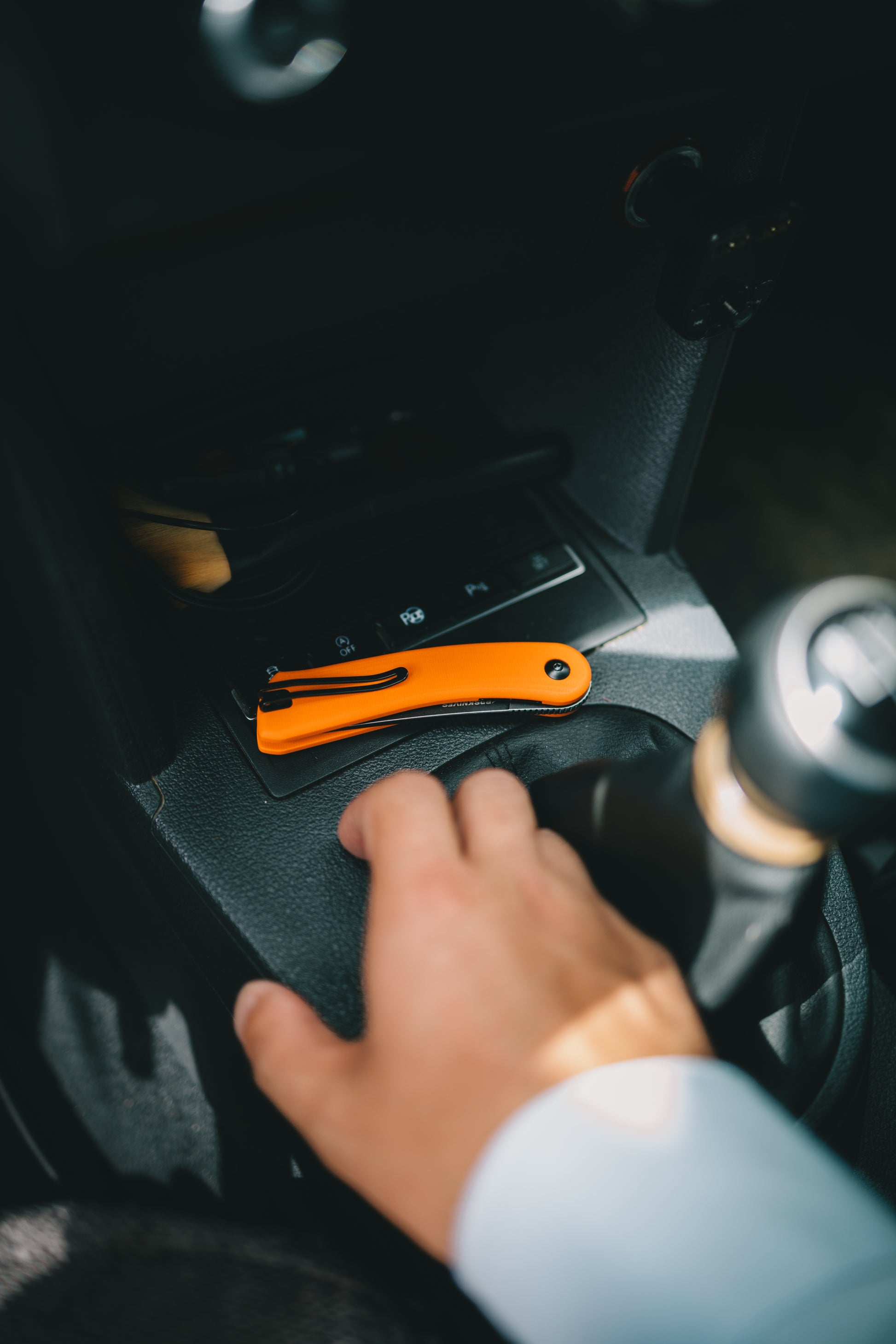 Hand reaching for an orange tool kit inside a car.