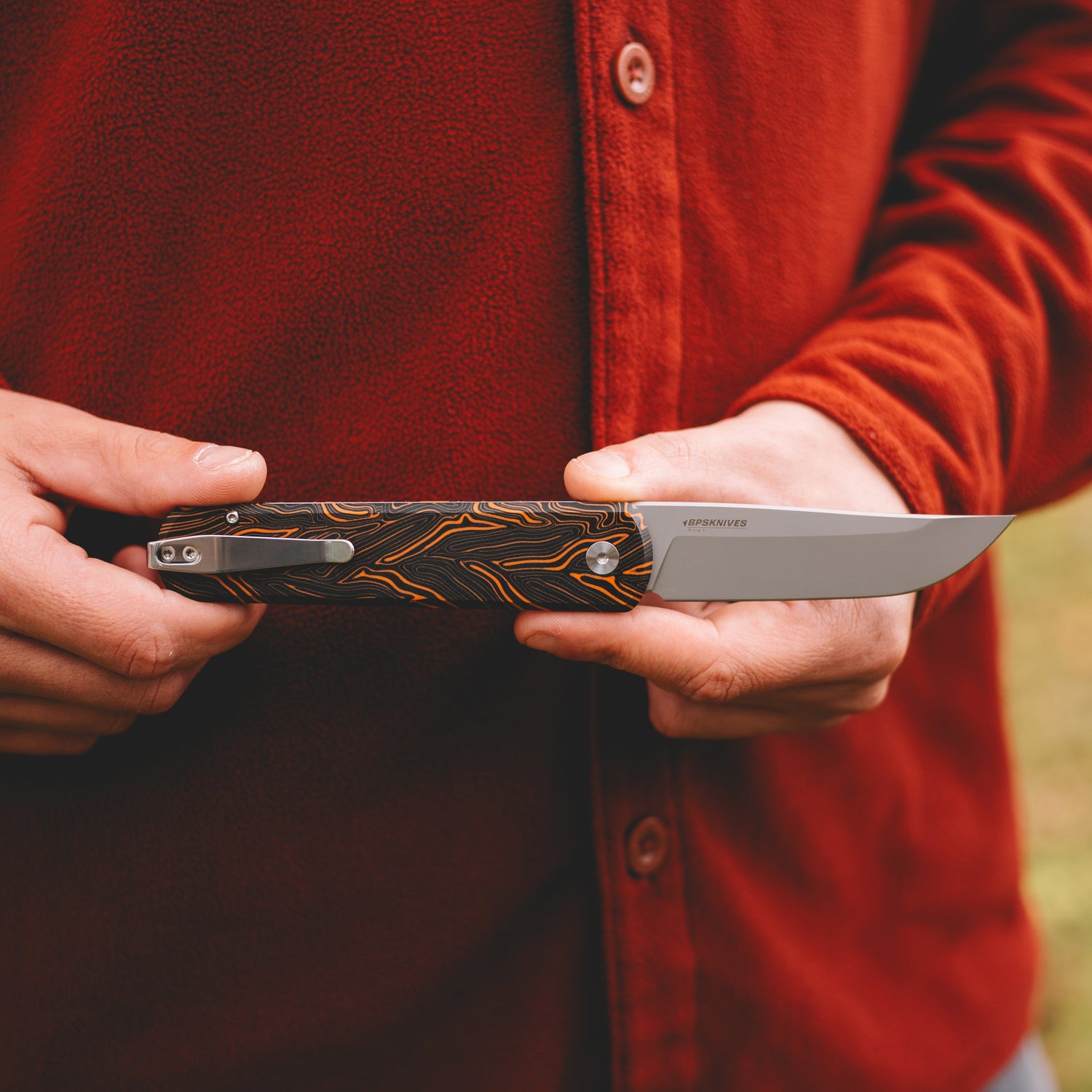 Person holding a folding knife with a detailed handle in an outdoor setting