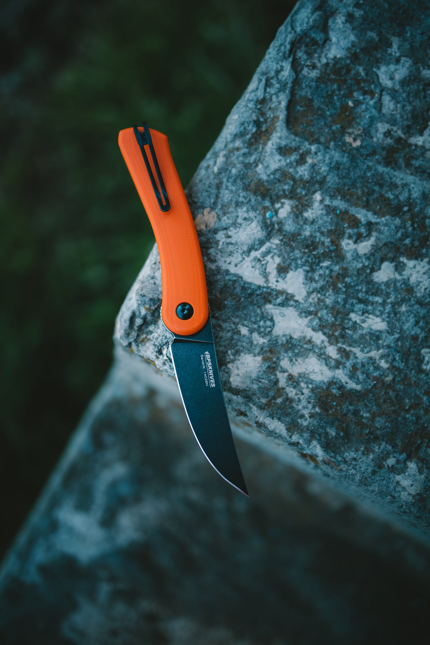 Orange folding knife on a textured stone surface with a blurred green background
