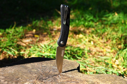 Folding knife on a wooden stump with grass in the background